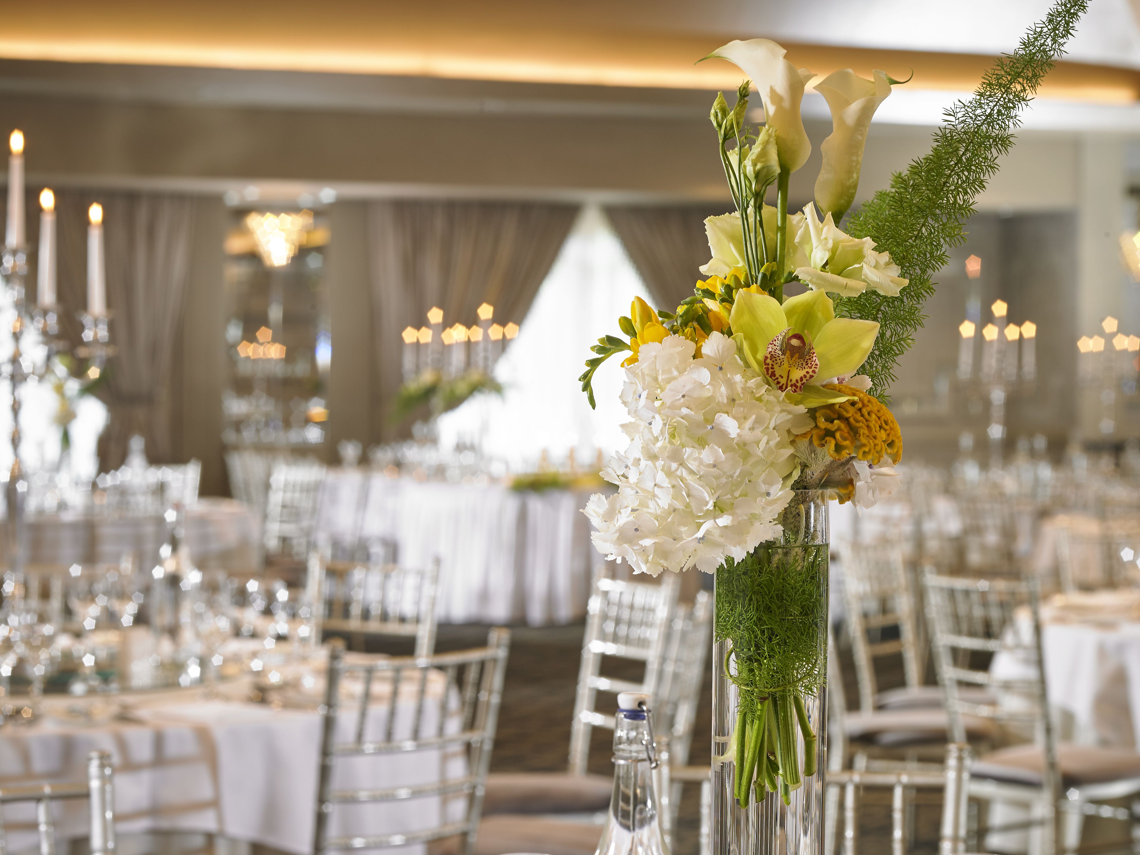 A banquet hall with tables set for a formal event, featuring floral centerpieces and candlelit ambiance.