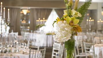 A banquet hall with tables set for a formal event, featuring floral centerpieces and candlelit ambiance.
