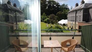 A balcony with wicker chairs and a table, overlooking a garden with white tents and a pathway.