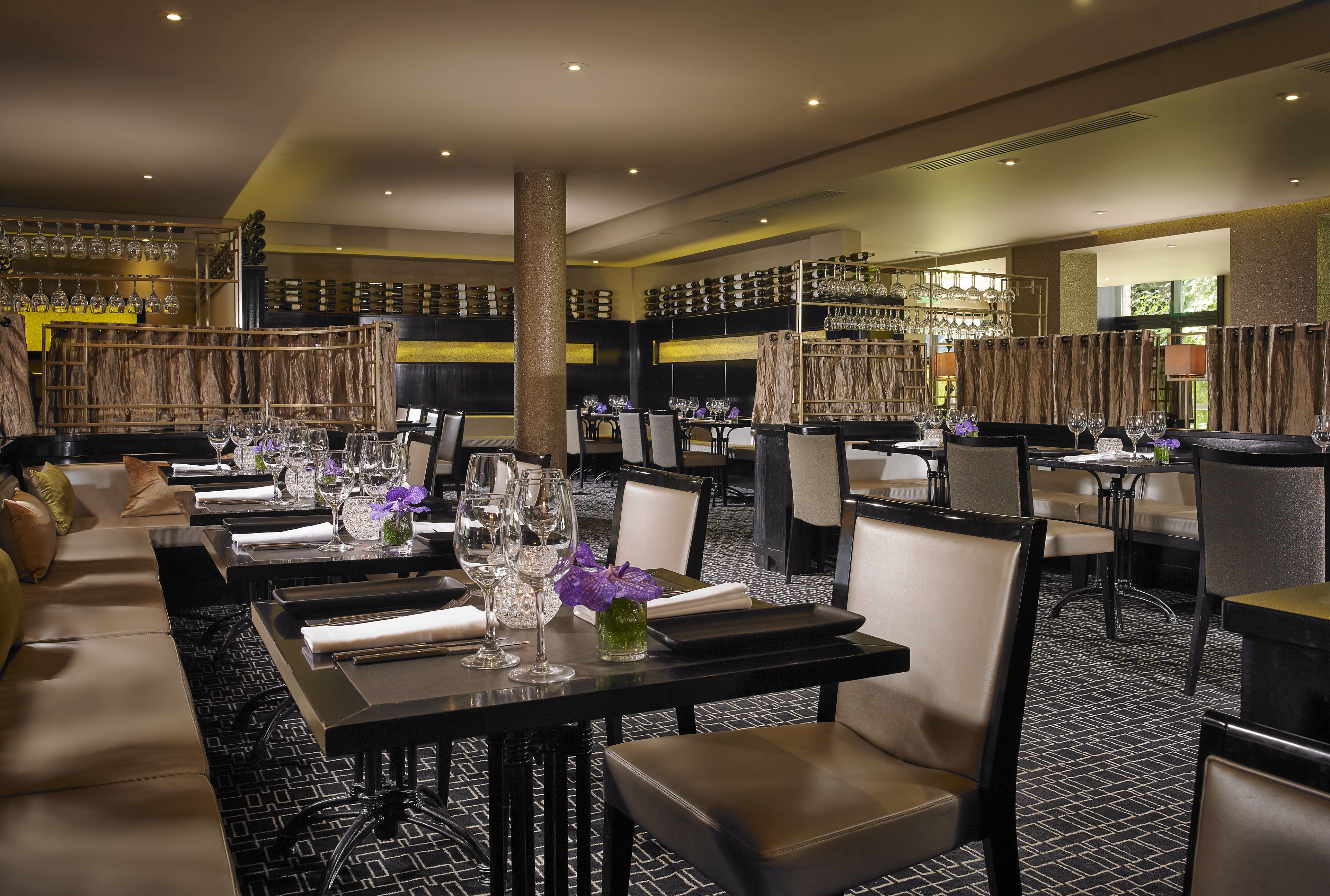 Un restaurant doté de nombreuses tables, de chaises et d’un bar, avec des étagères remplies de bouteilles et de verres.