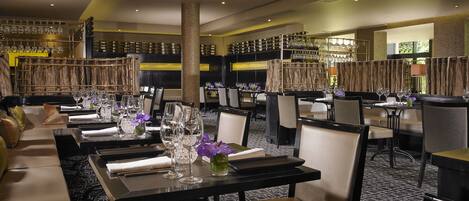A restaurant with multiple dining tables, chairs, and a bar area with shelves of bottles and glasses.