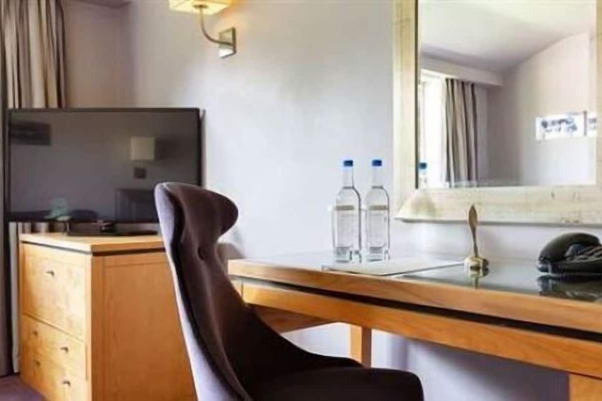 Hotelkamer met een houten bureau, een stoel, een spiegel, een telefoon, twee waterflesjes en twee groene appels.