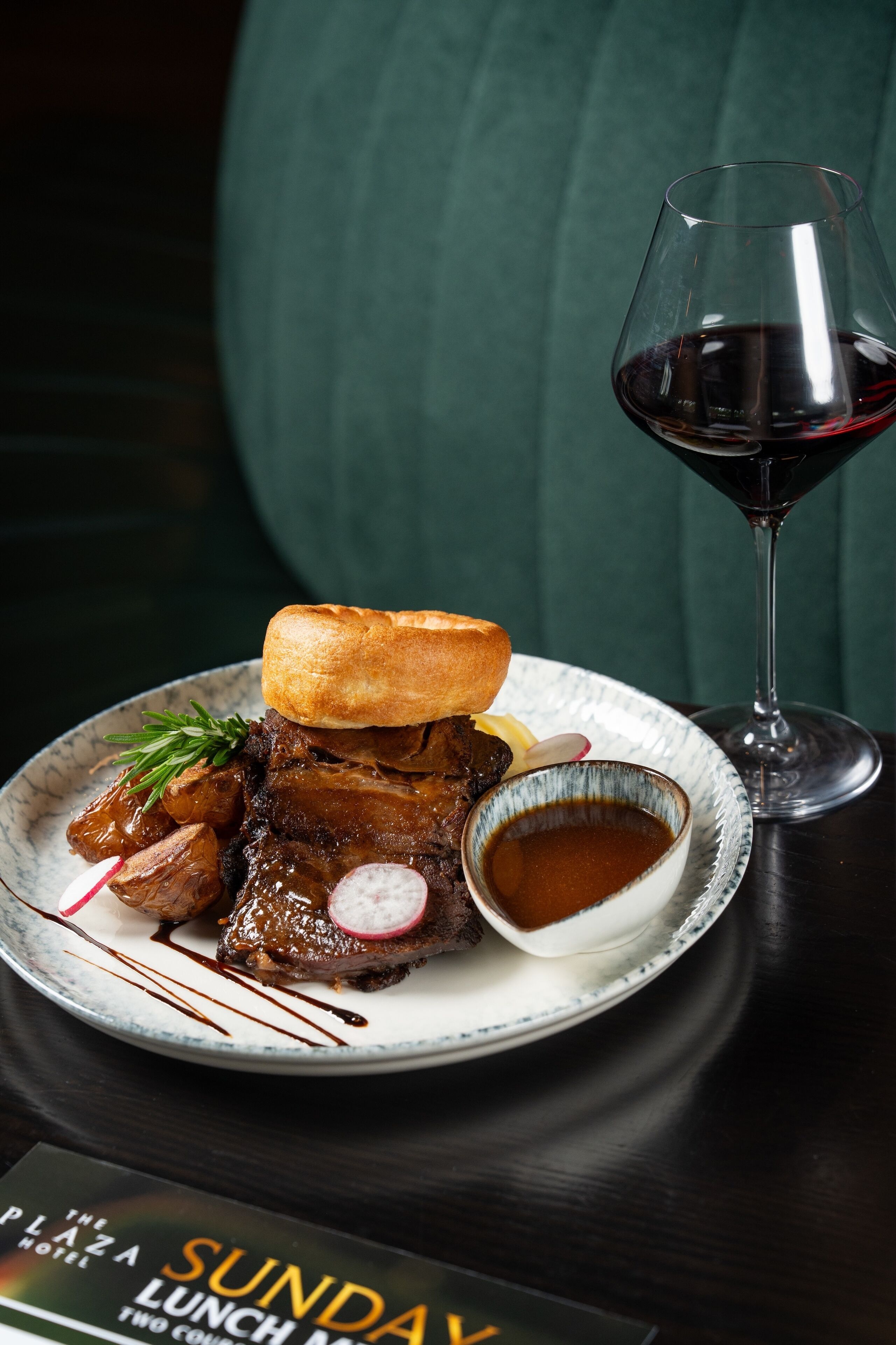 Une assiette de nourriture, un verre de vin rouge et un menu.