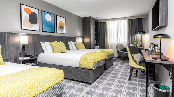 A hotel room with two beds, a desk, a chair, a TV, and artwork on the wall. - The Plaza Hotel (Dublin)