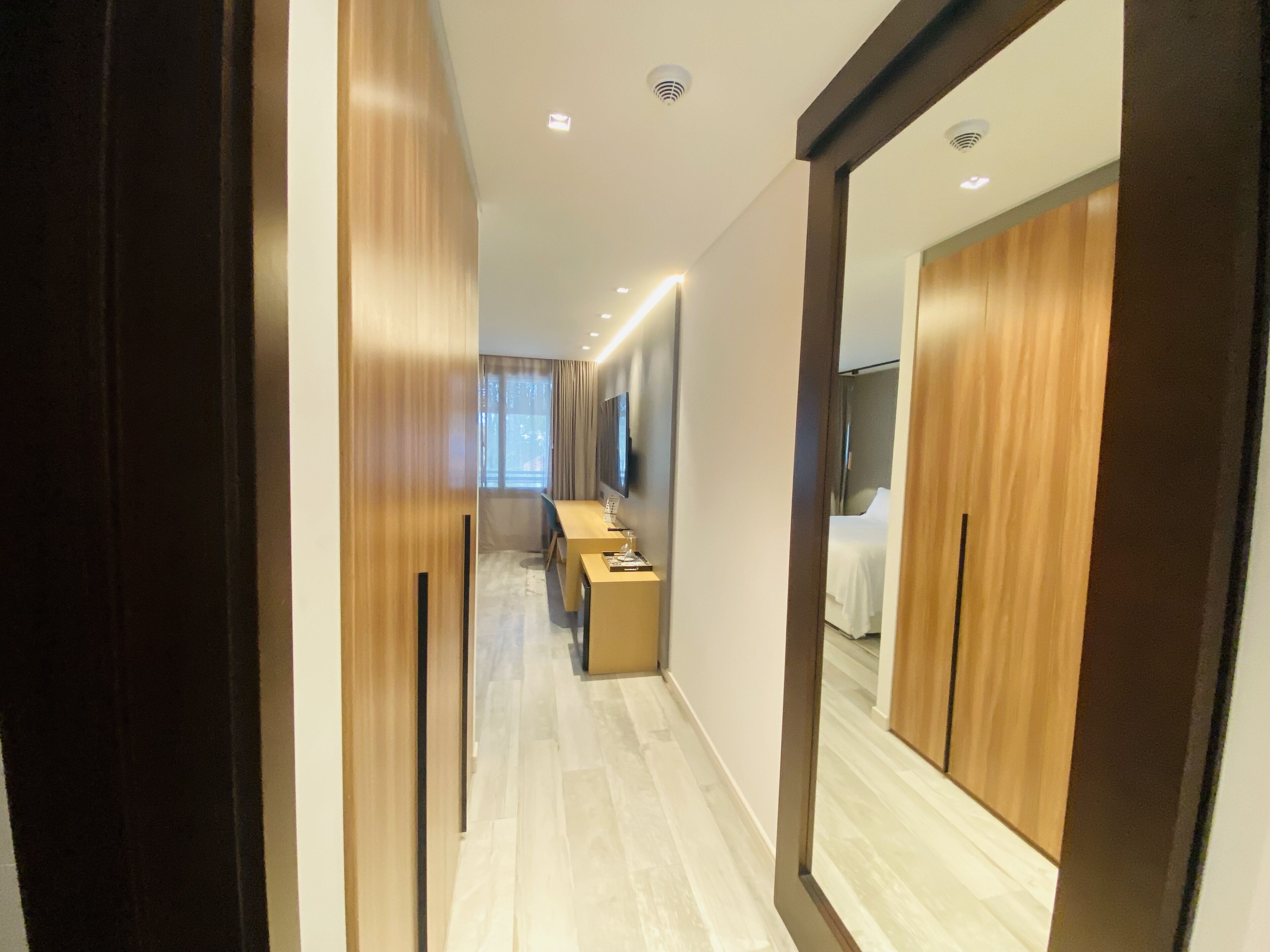 A hallway with wooden paneling, a desk with a computer, and a bed in the room.