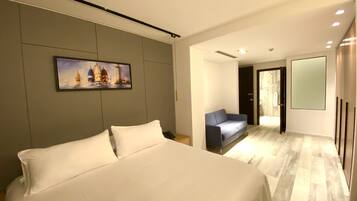 Una habitación de hotel moderna con una cama grande, un sofá azul, un cuadro de veleros y un espejo amplio.