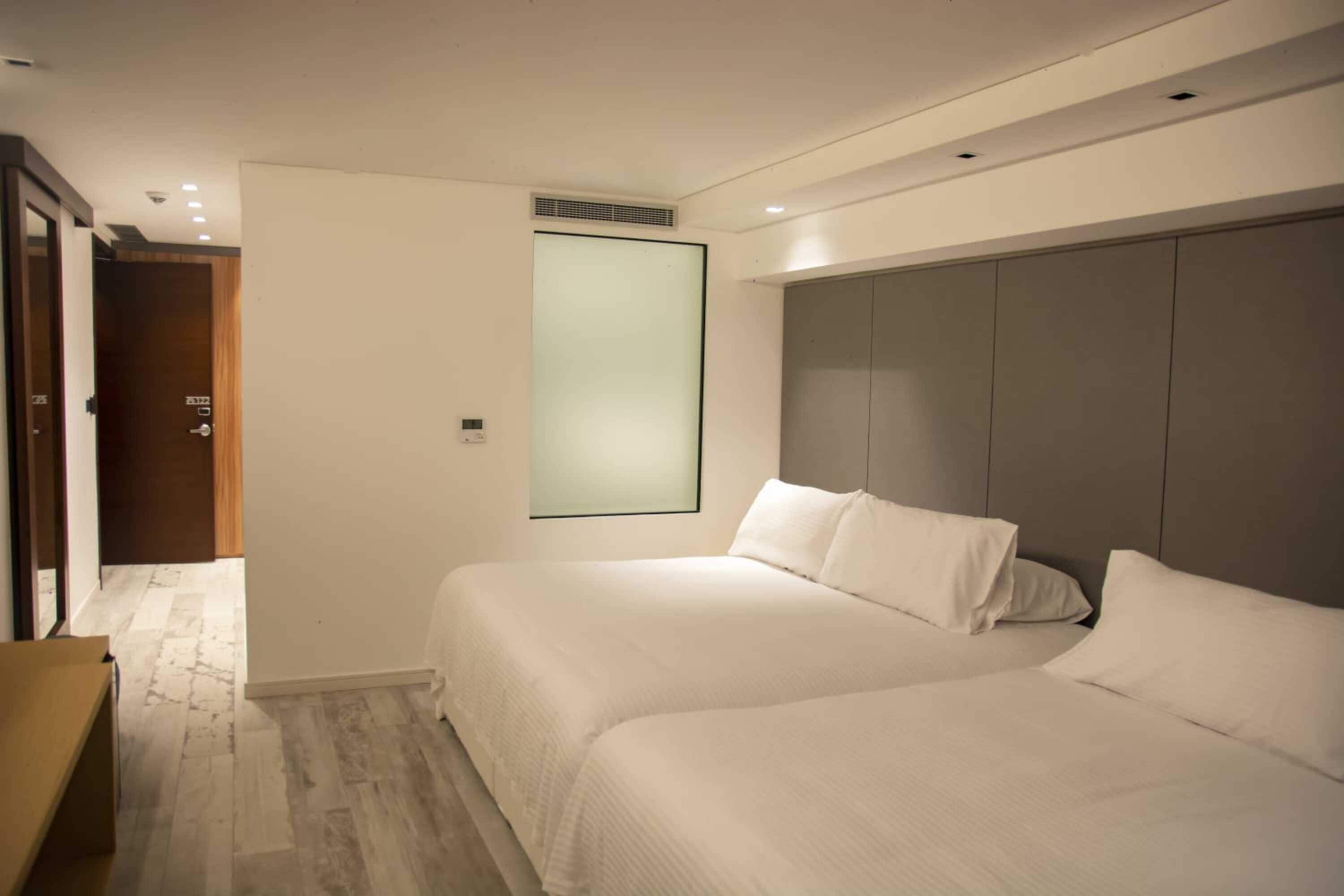 A hotel room with two beds, a large wardrobe, and a door leading to another room.