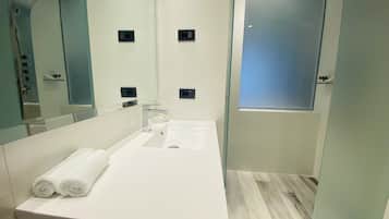 A modern bathroom with a white sink, two towel rolls, a mirror, and a glass partition.