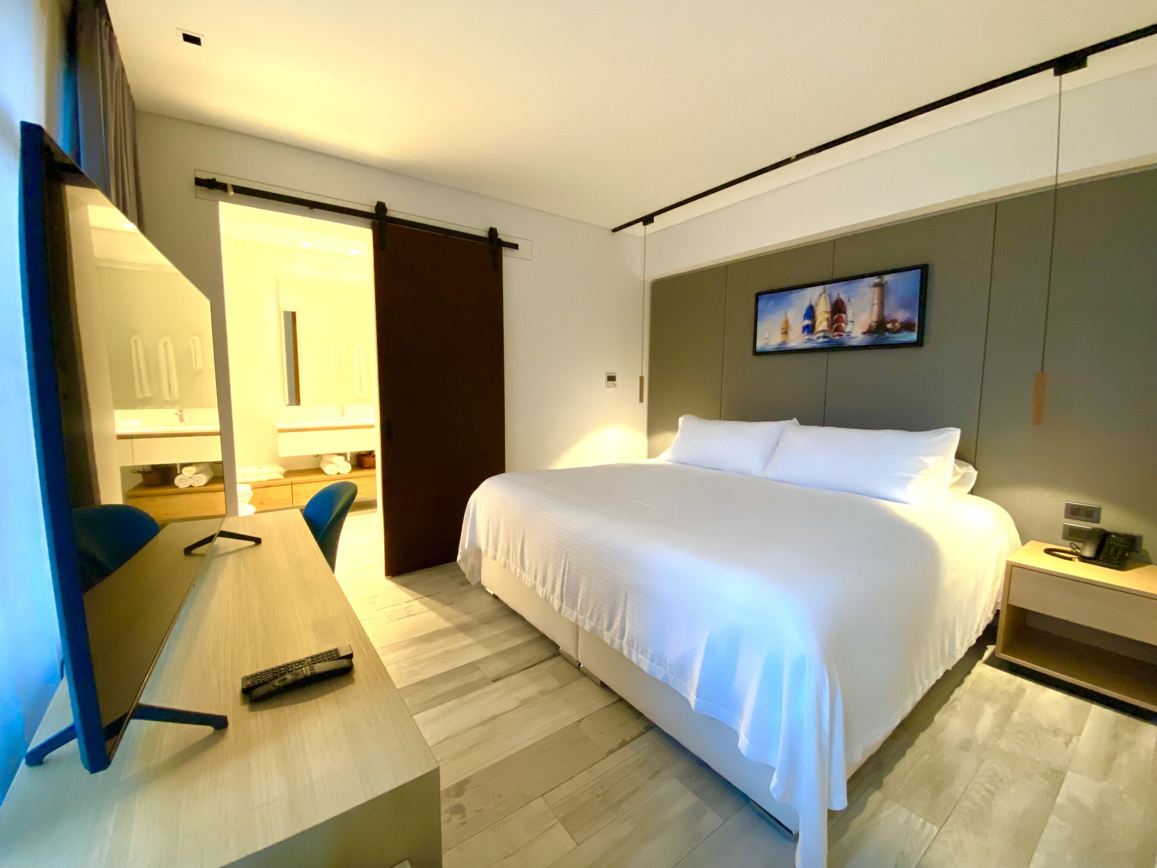 Une chambre d’hôtel comprenant un lit, un bureau, une chaise, une lampe de bureau, une table de chevet avec un téléphone et un tableau accroché au mur.