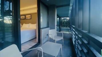 Une chambre d’hôtel moderne avec un balcon, un lit et deux chaises blanches.