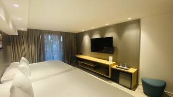 Habitación de hotel moderna con dos camas grandes, un televisor de pantalla plana, un escritorio de madera y una pequeña zona de estar.