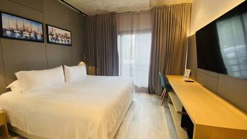 A hotel room with a large bed, a desk, a TV, and two paintings on the wall.