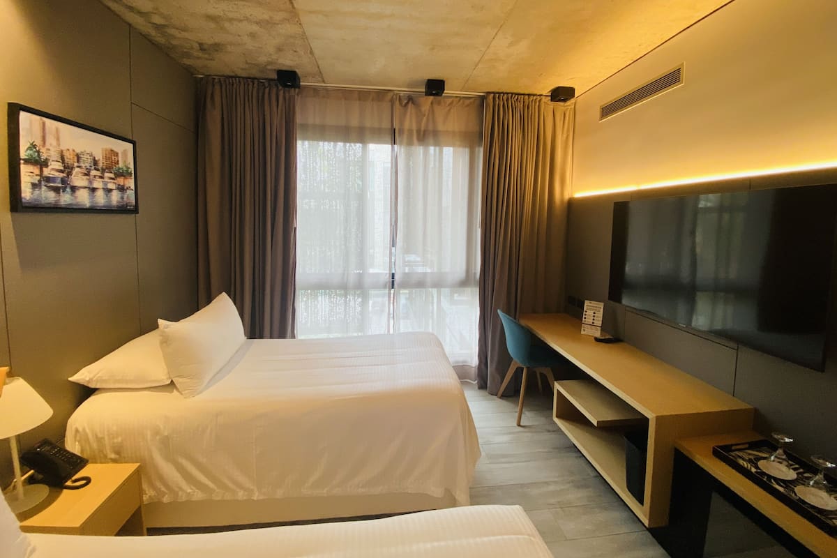 A hotel room with a bed, a desk, a TV, and a window with curtains.