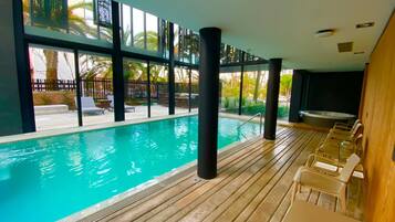 An indoor swimming pool with clear views of palm trees and a fence outside.