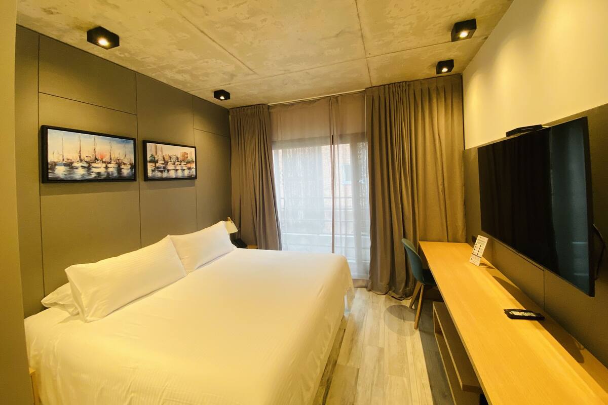A hotel room with a large bed, a desk with a flat-screen TV, and two framed pictures on the wall.