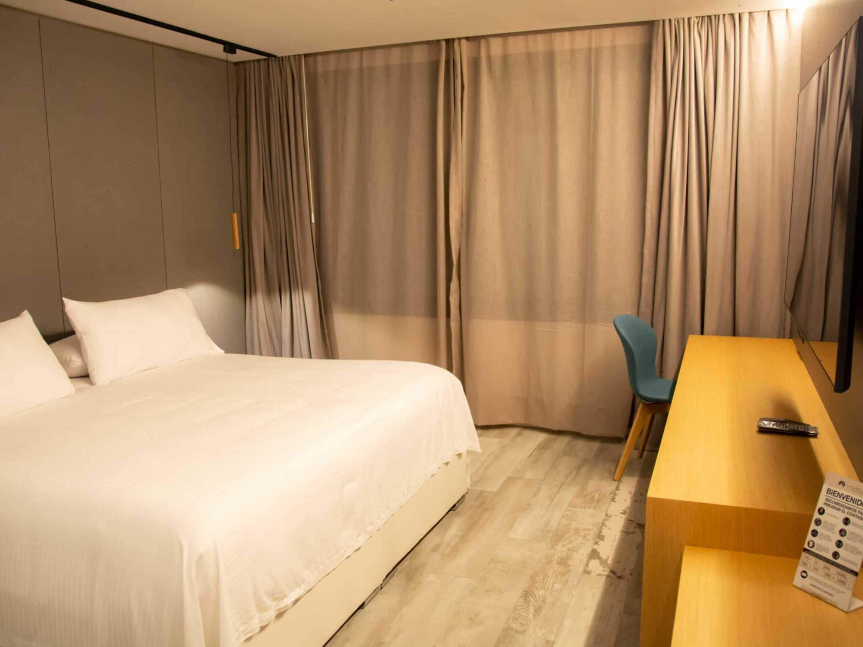 A hotel room with a large bed, a desk with a chair, and a TV.