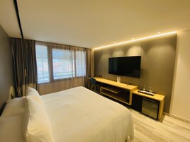 A hotel room with a bed, a desk, a TV, and a window with curtains.