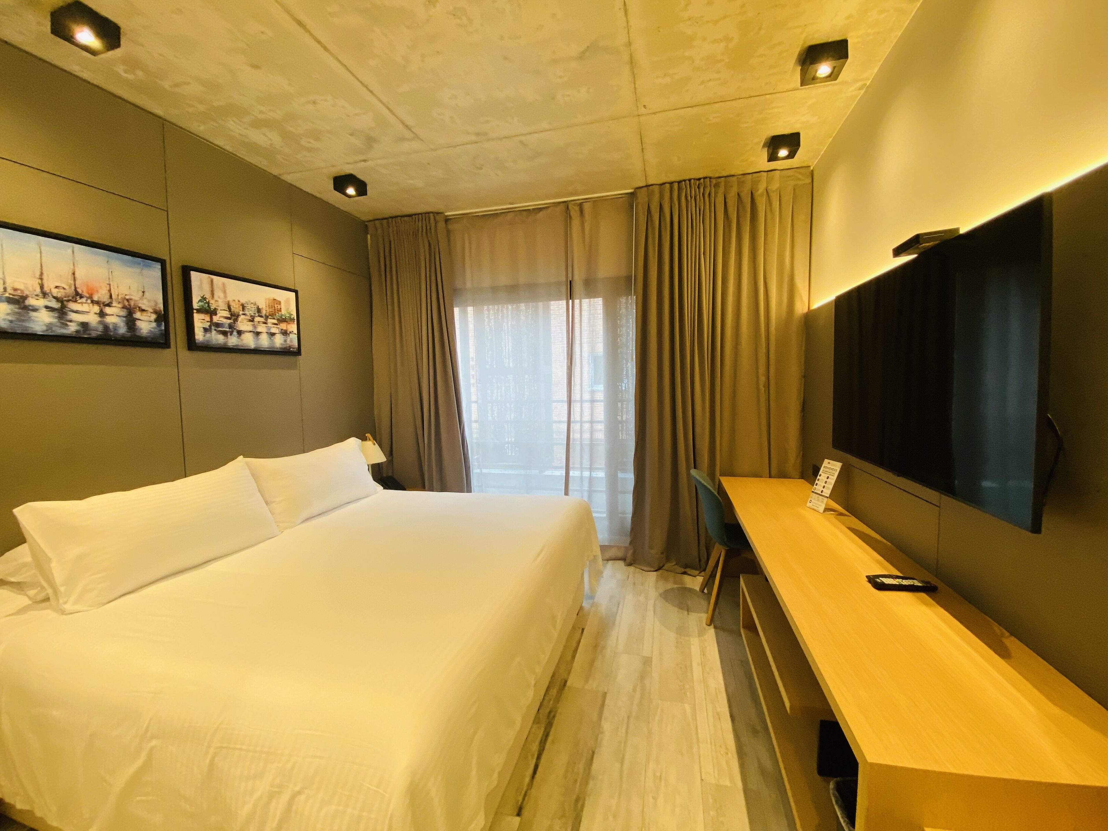 Una habitación de hotel con una cama grande, un escritorio, un televisor de pantalla plana y dos cuadros en la pared.
