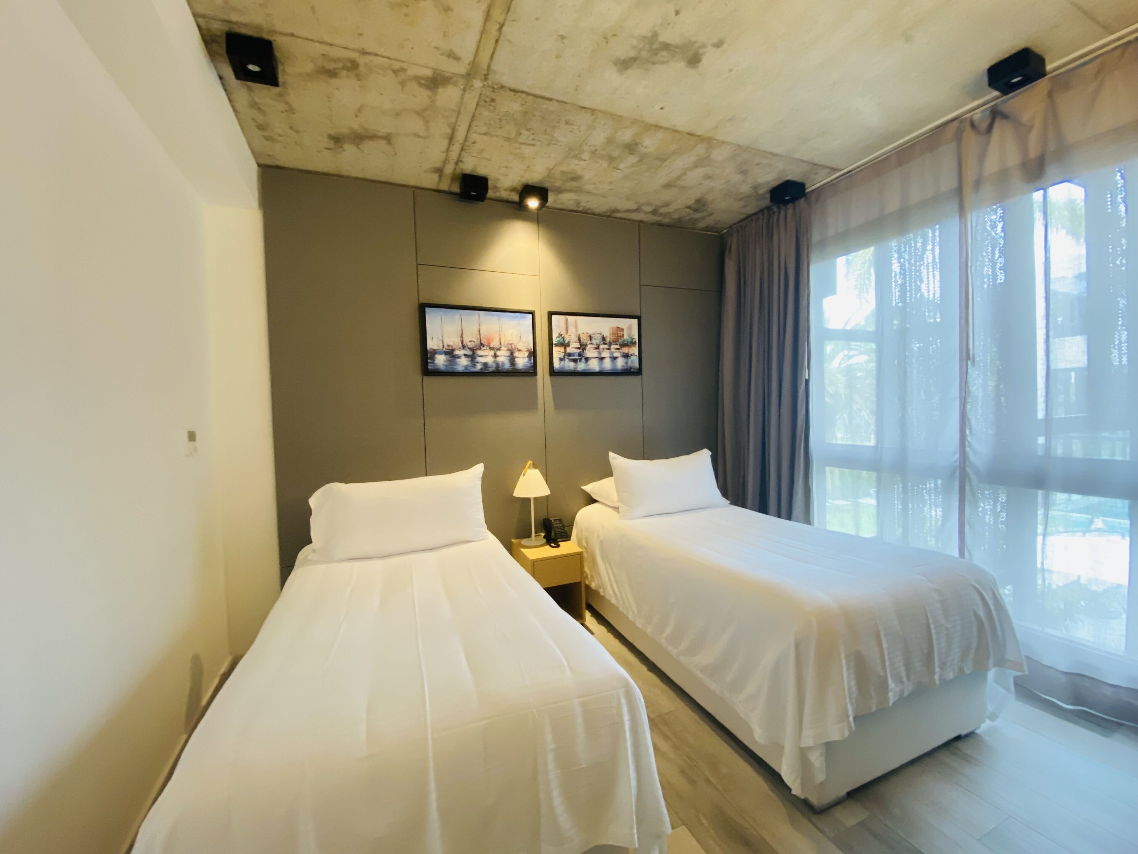 A hotel room with two beds, a nightstand with a lamp, and two framed pictures on the wall.
