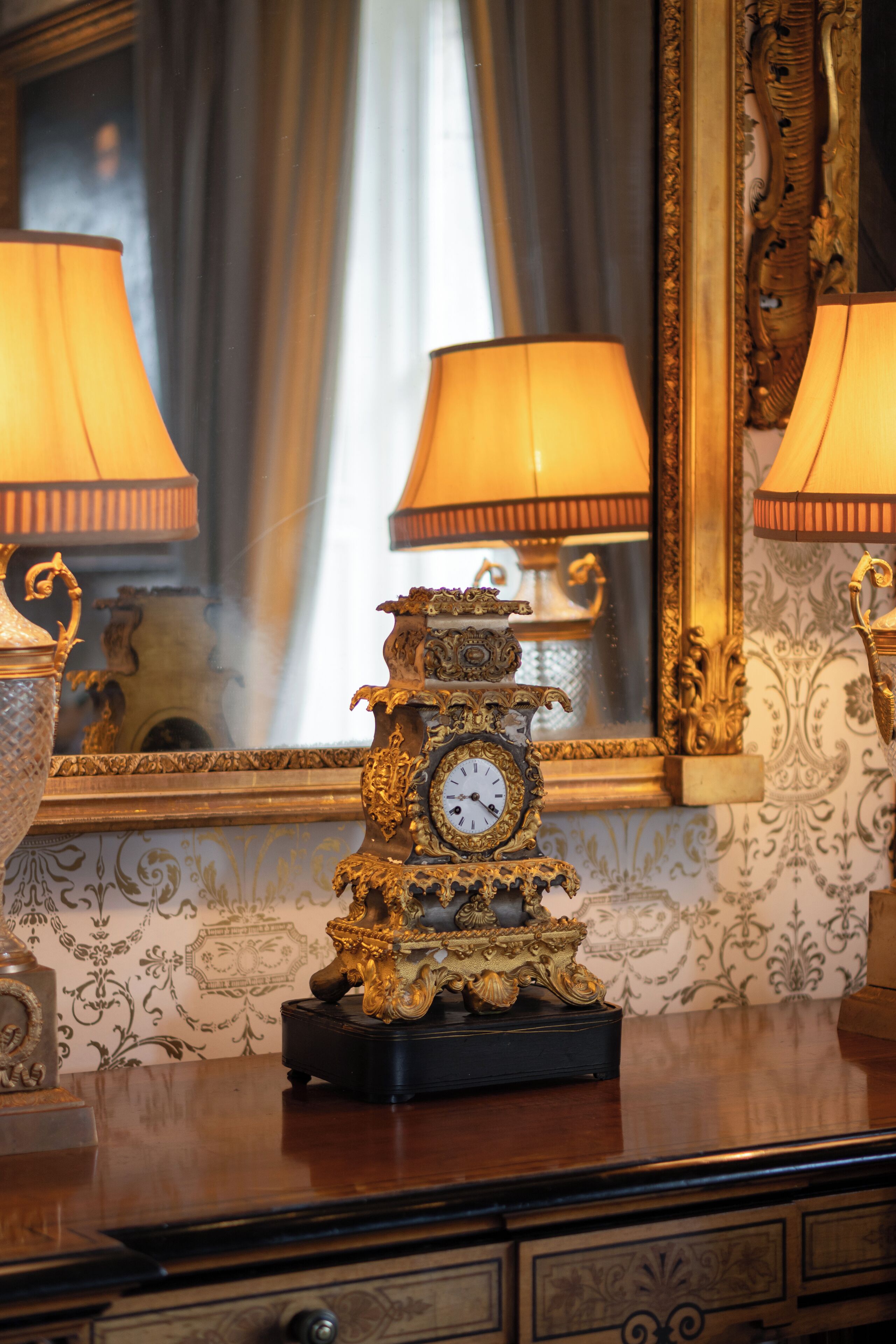 A luxurious room with ornate furniture, including a decorative clock and lamps, and a mirror reflecting the room's decor.