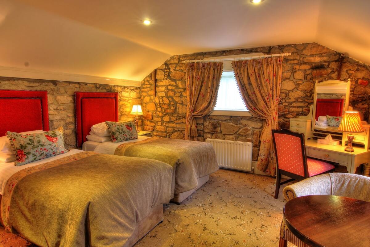 Ein Zimmer mit zwei Betten, einem Schreibtisch, einem Stuhl, einem Spiegel und einem fenster mit Vorhängen.