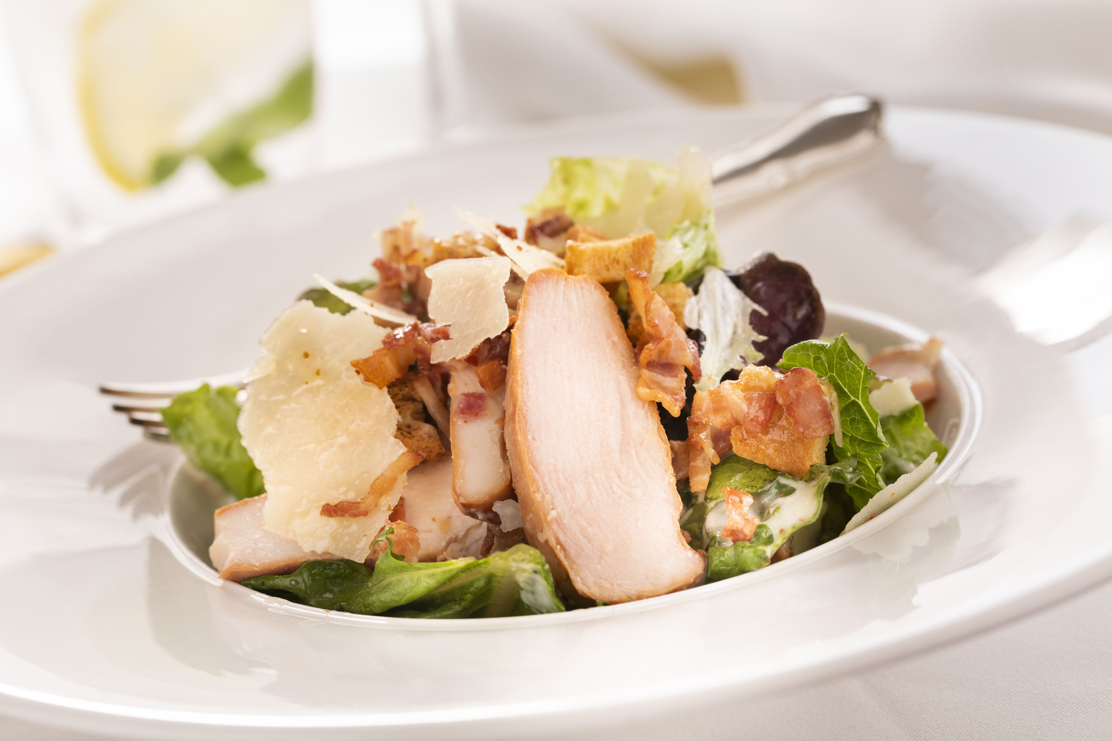Un plato blanco con ensalada de lechuga, crutones y trozos de pollo.