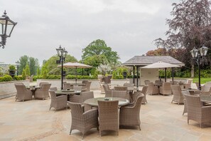 An outdoor patio with wicker furniture and umbrellas, surrounded by greenery and a gazebo. - Cabra Castle Hotel (Kingscourt)