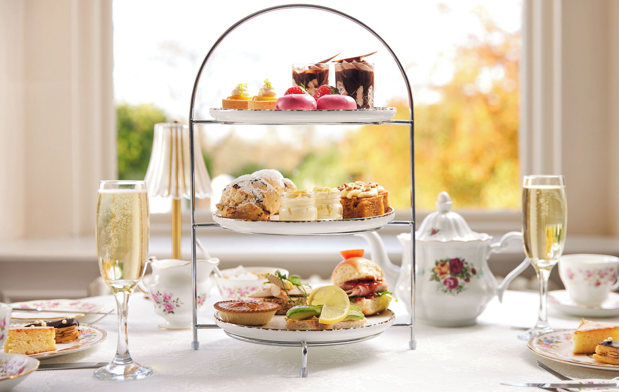 A three-tiered dessert stand with various pastries and a teapot on a table.