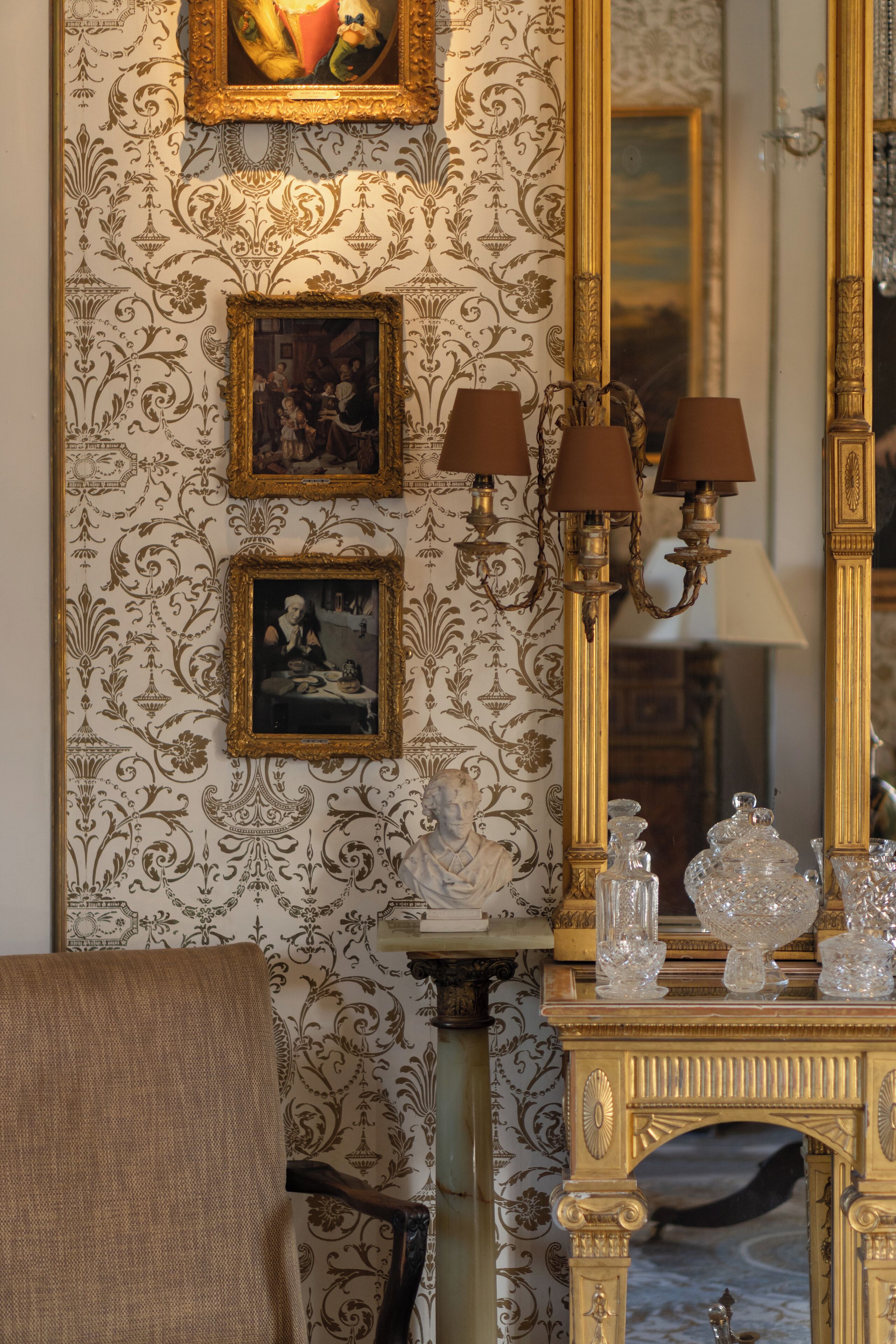 Una habitación con papel tapiz ornamentado, un espejo grande y una consola con objetos decorativos.