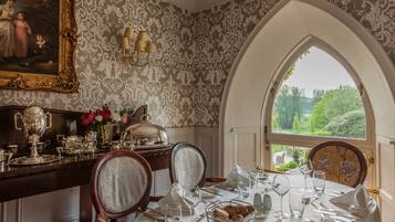 Comedor con una mesa preparada para cuatro personas, un candelabro y vistas a través de un ventanal arqueado.