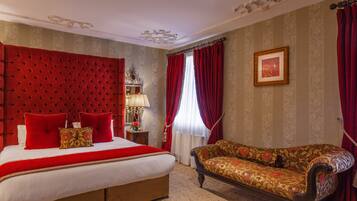A bedroom with a large bed, red curtains, a sofa, and a chandelier.