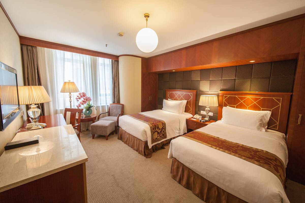 Habitación de hotel con dos camas, un escritorio, una silla, una lámpara y una ventana con cortinas.