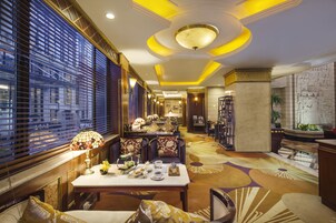A hotel lobby with a dining area, a reception desk, and a large window with blinds.