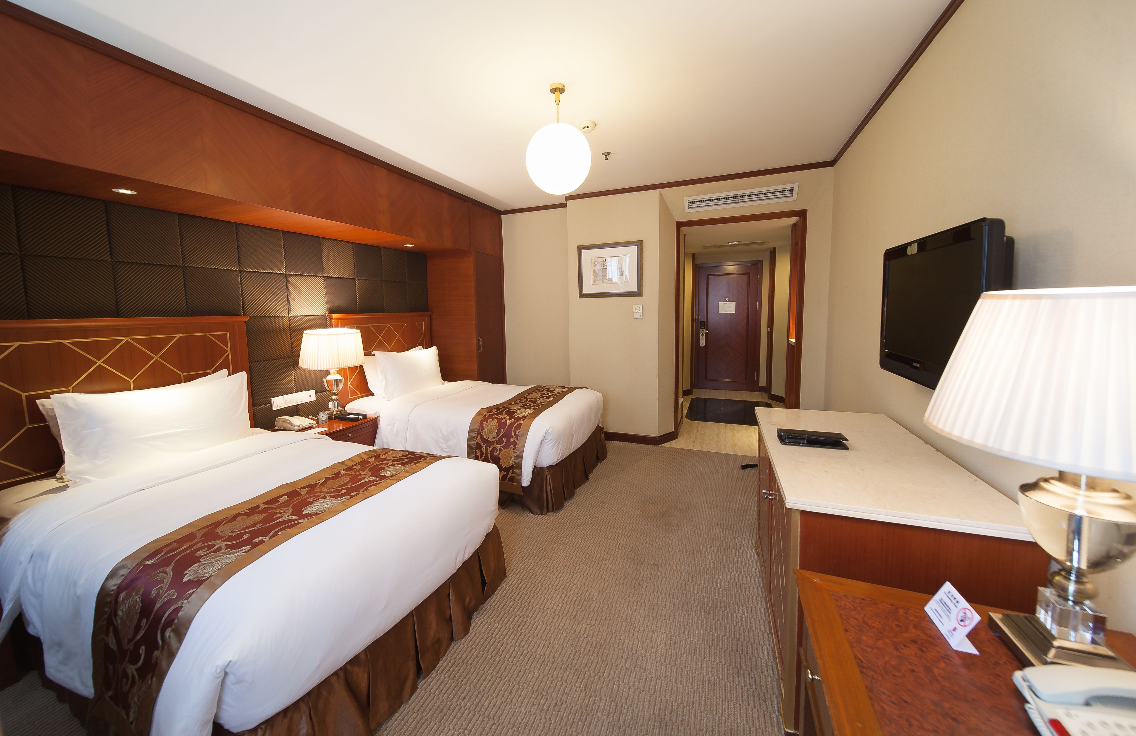 A hotel room with two beds, a desk, a TV, and a lamp.