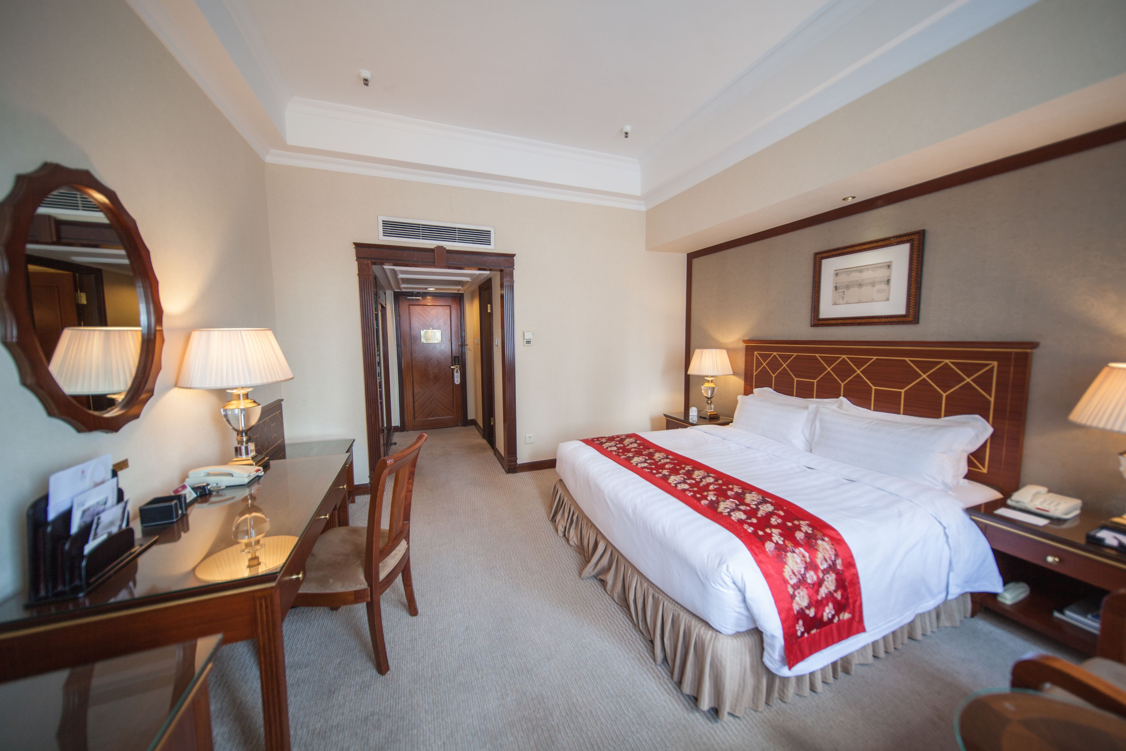 A hotel room with a large bed, a desk with a lamp, a chair, and a mirror.