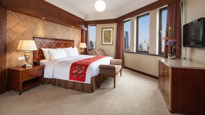 Una camera d'albergo con un letto grande, una scrivania con una lampada, una sedia, una televisione e vista sulla città da ampie finestre.