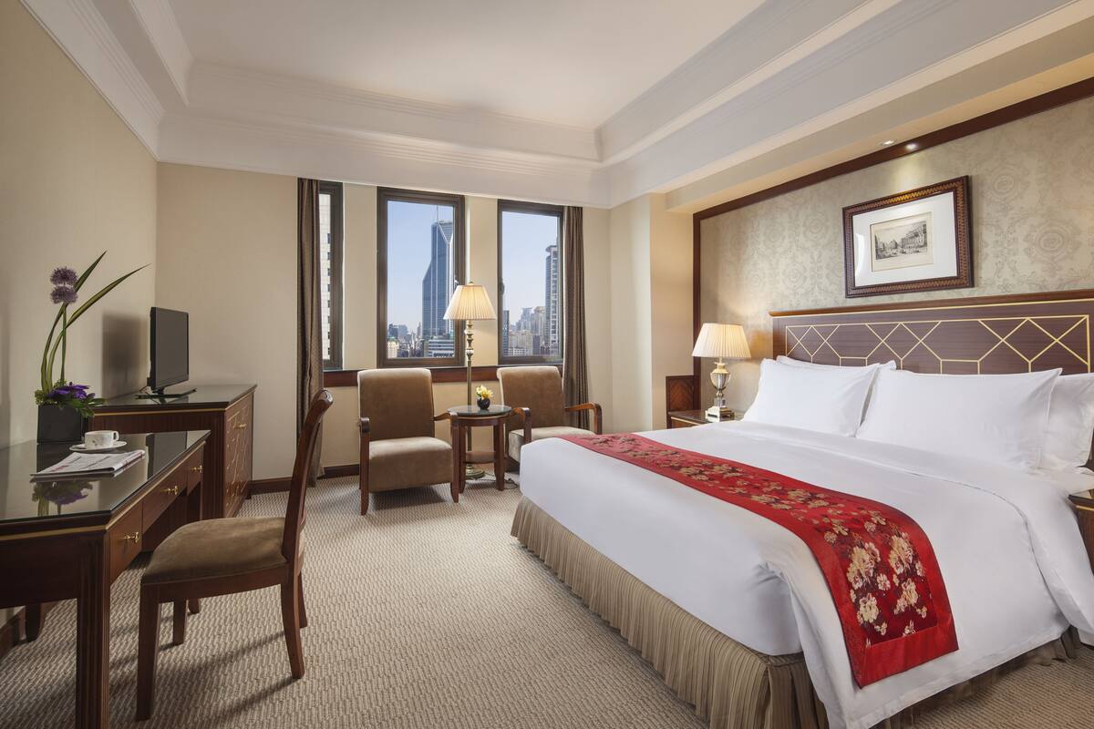 Habitación de hotel con una cama grande, un escritorio, dos sillas, un televisor y vistas a la ciudad.