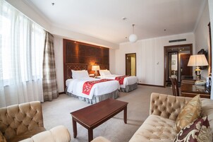 A hotel room with two beds, a sitting area with a sofa and a table, and a large window with curtains.
