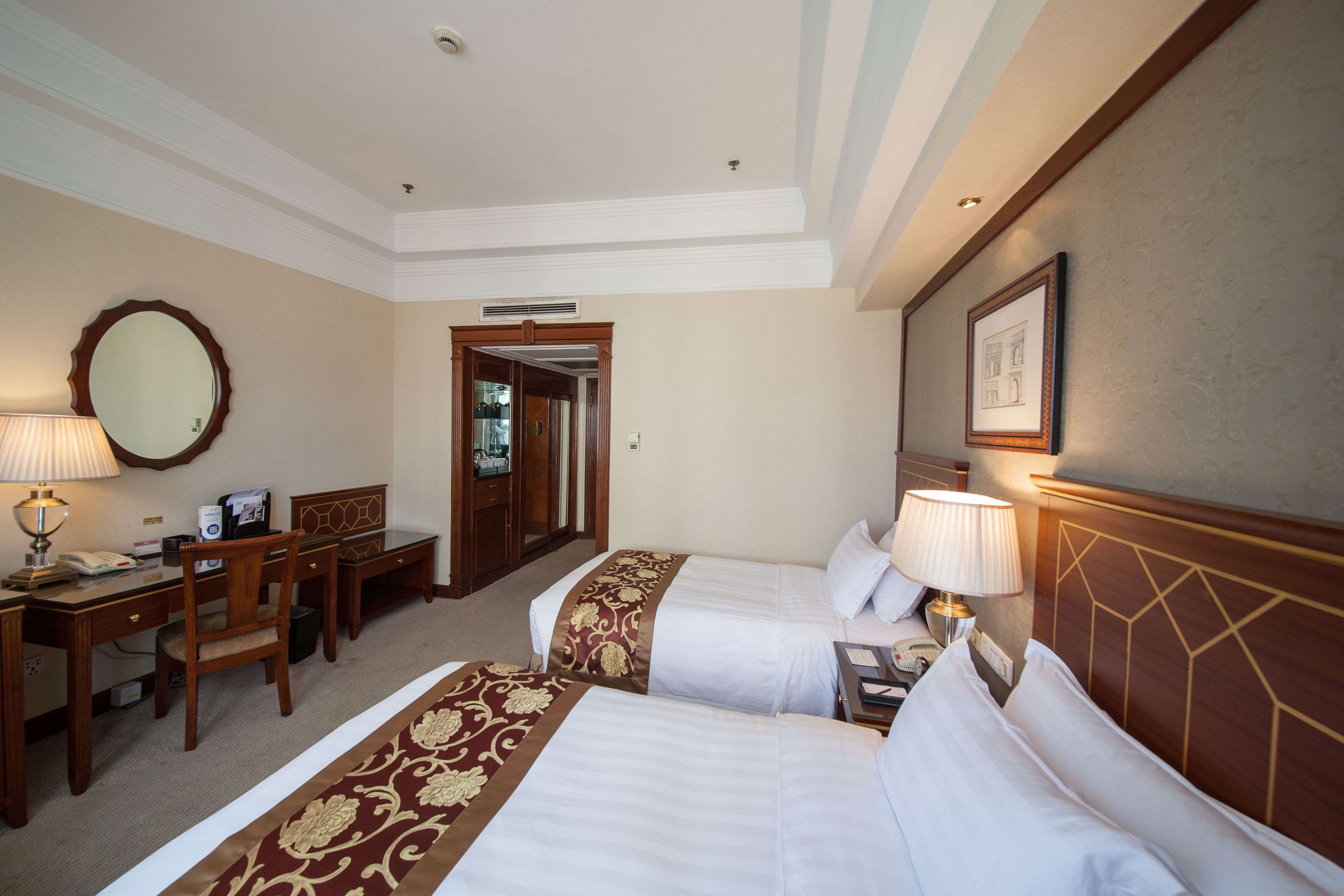 A hotel room with two beds, a desk, a chair, a lamp, and a mirror.