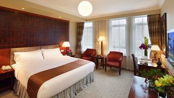 A hotel room with a large bed, two armchairs, a small table, and a desk with a lamp.