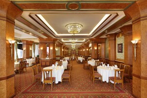 A formal dining room with multiple tables and chairs, chandeliers, and wall sconces.