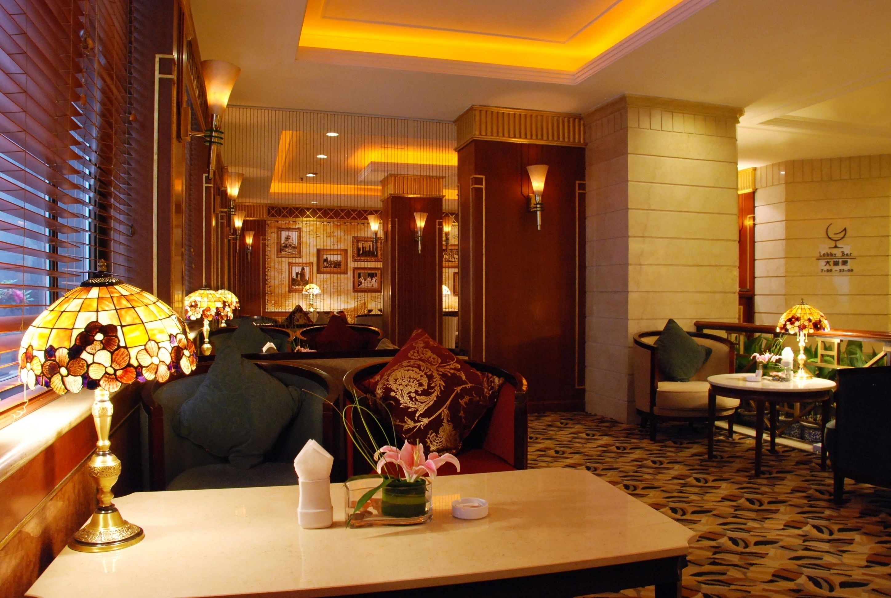 A lobby with a seating area, a table with a lamp, and a decorative vase with flowers.