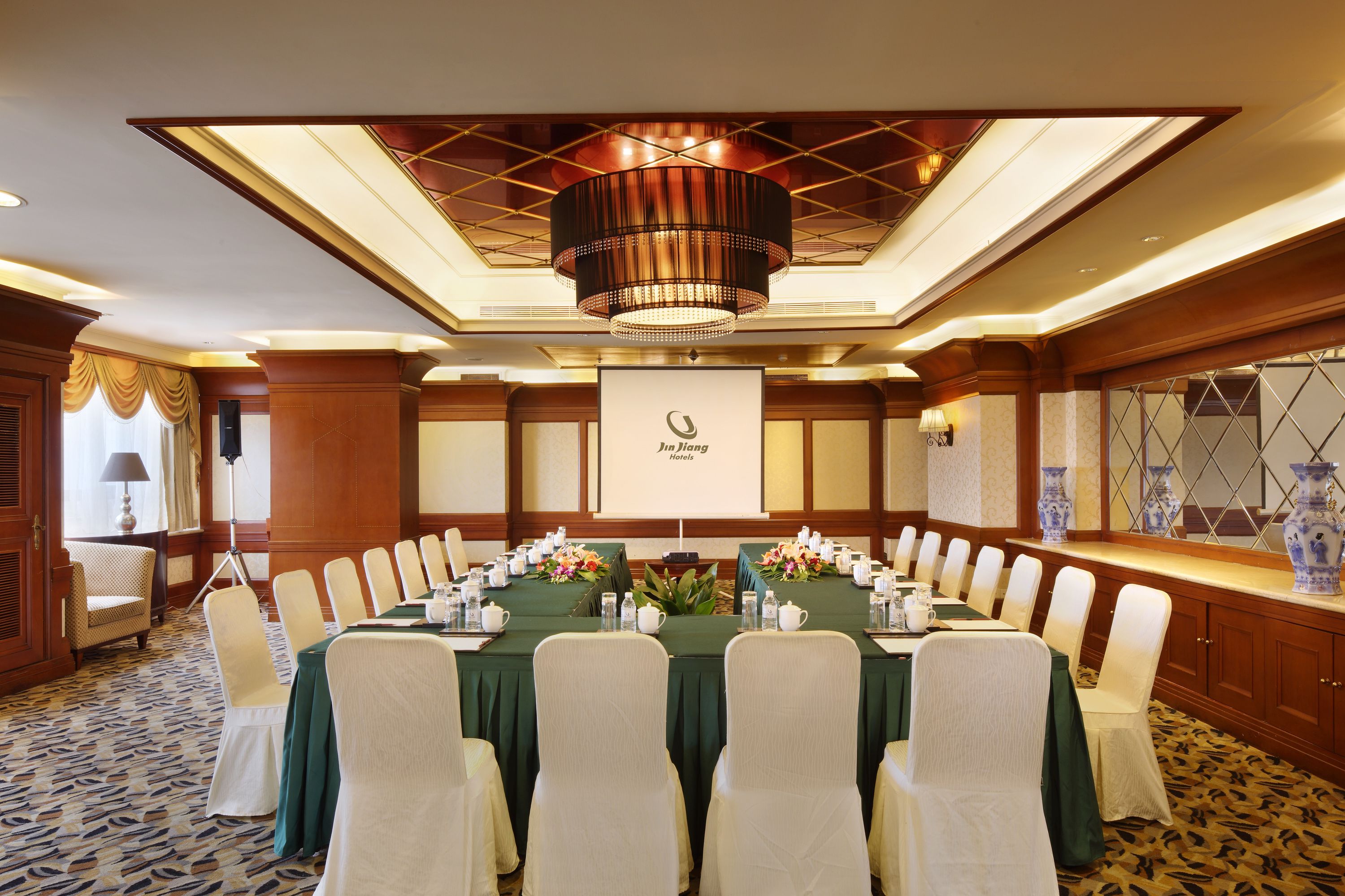 A conference room with a long table, white chairs, and a chandelier.