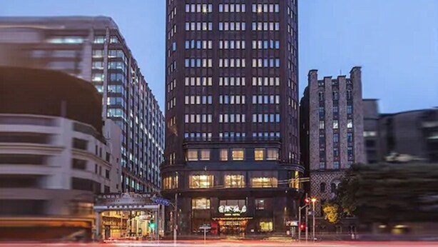 Un edificio alto e moderno con un design architettonico distintivo, caratterizzato da una sezione superiore illuminata e di grande impatto.
