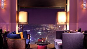 A modern lounge with two armchairs, a round table, and a city view. - Pan Pacific Hanoi (Hanoi)