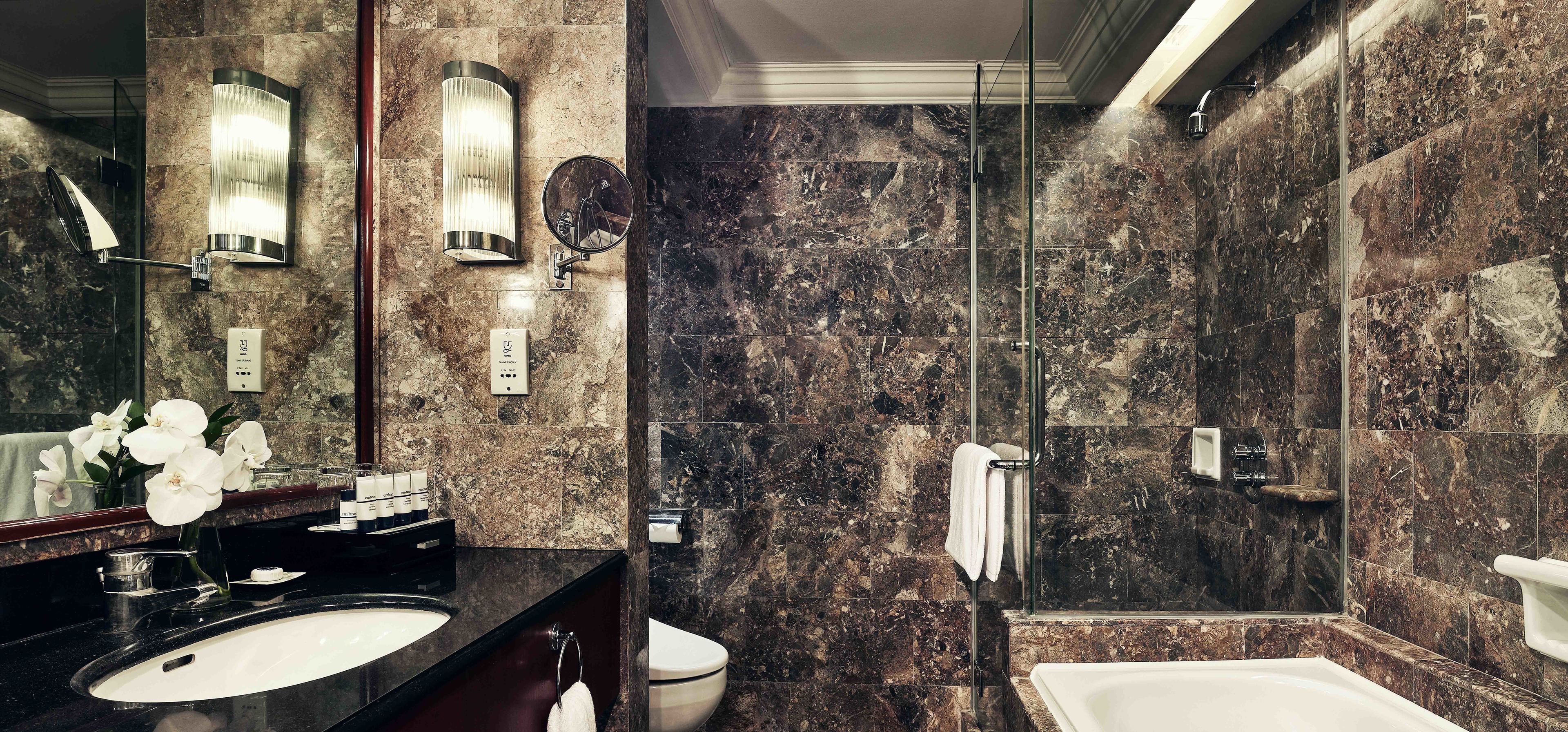 A modern bathroom with a marble wall, a glass shower enclosure, a sink, and a toilet.