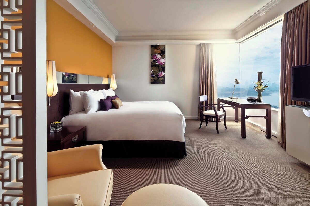 A hotel room with a large bed, a desk, a chair, and a TV.