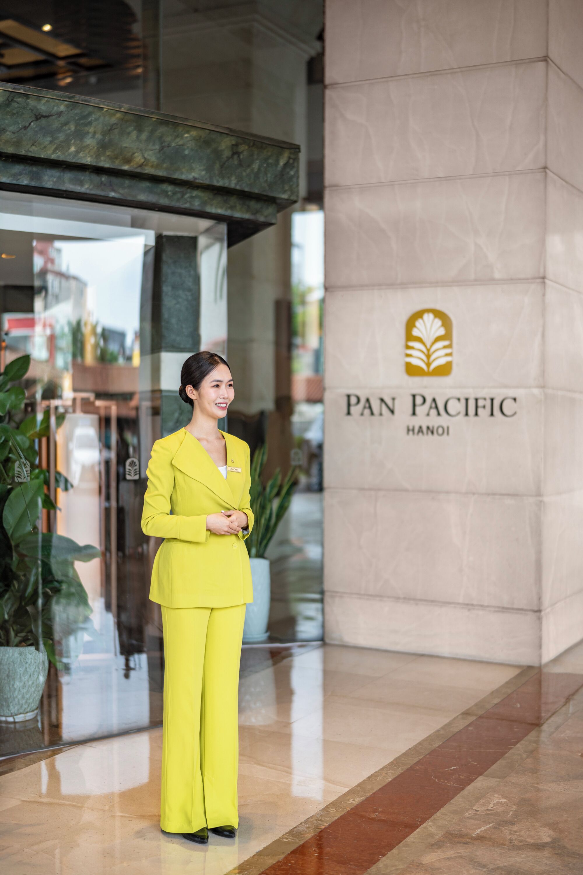 A woman in a yellow suit standing in front of a Pan Pacific Hanoi sign.