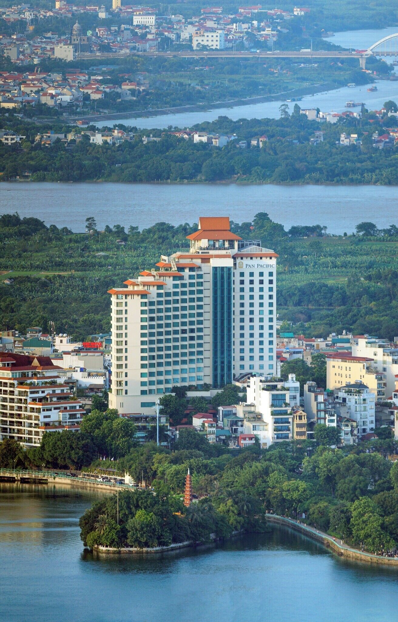 A high-rise hotel with a modern design, located near a body of water with a bridge in the background.