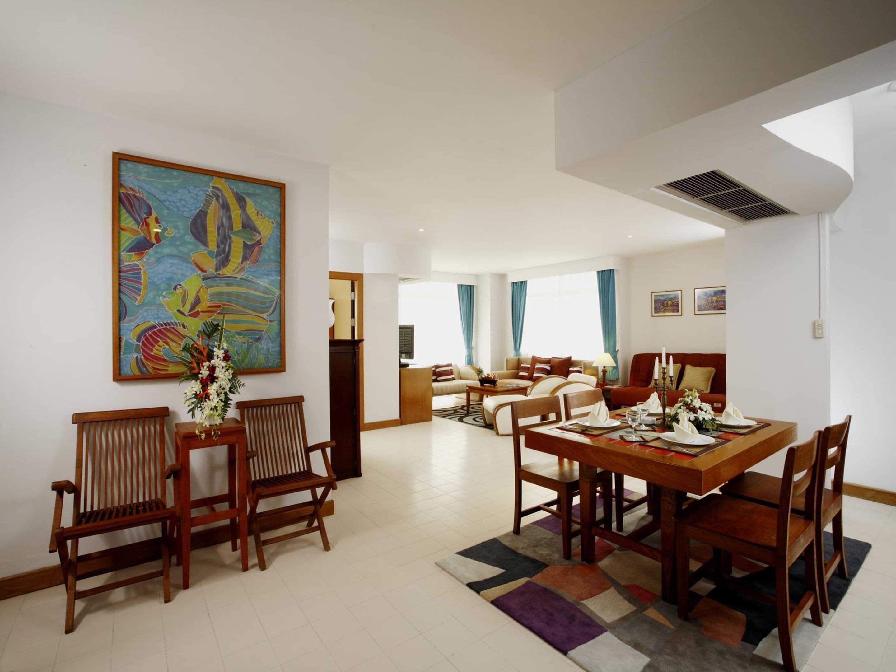 A spacious living area with a dining table set for four, a sofa, and a large painting on the wall.